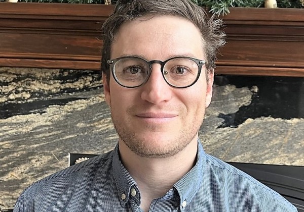 A man with brunette hair with glasses smiling at camera. 