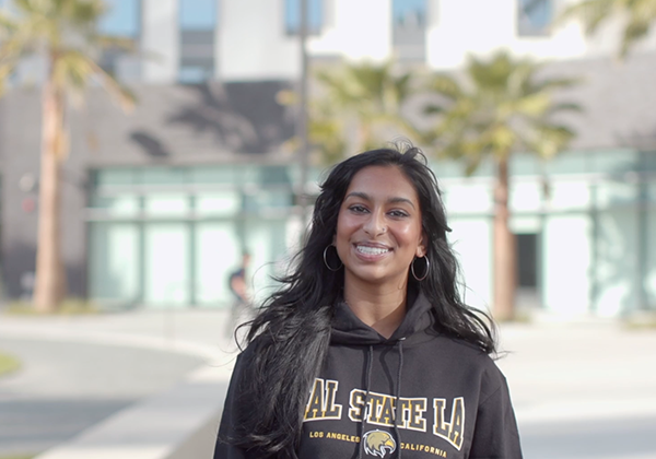 A person smiling and standing outdoors in front of a new building.