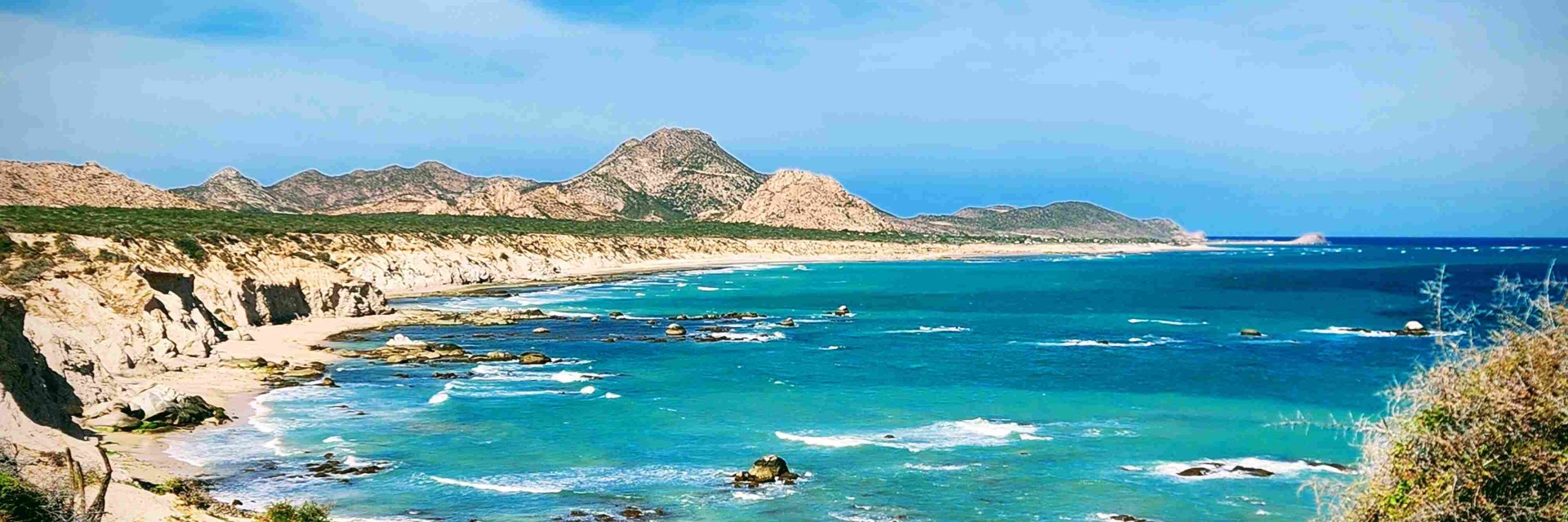 Overview of the coast meeting a bay with blue skies and wispy clouds.