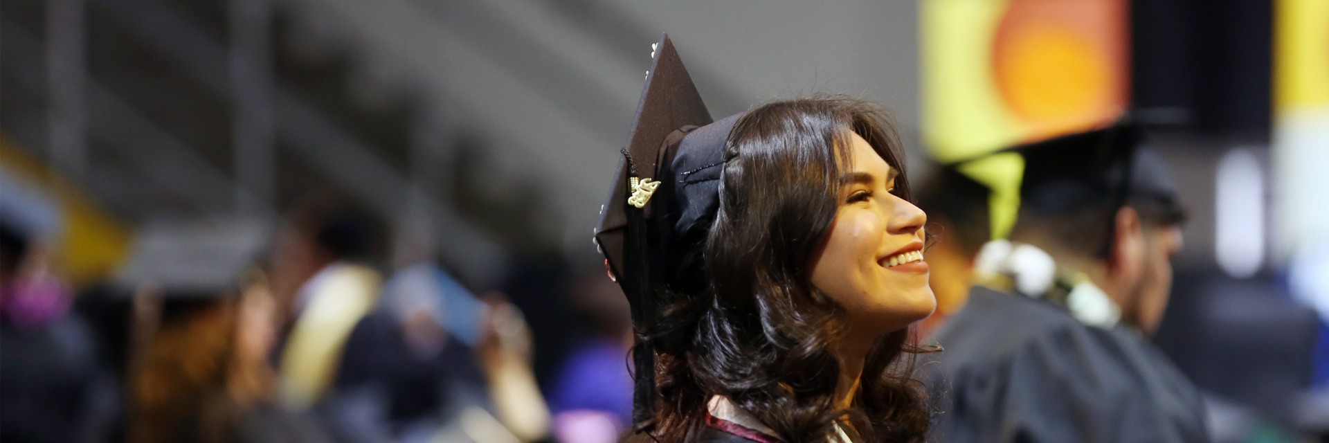 Graduating student in cap and gown smiles and looks in distance