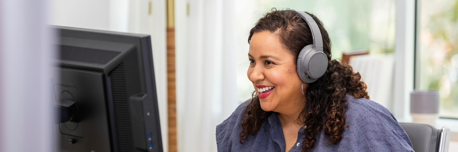 Woman uses desktop computer wearing headphones during online class.