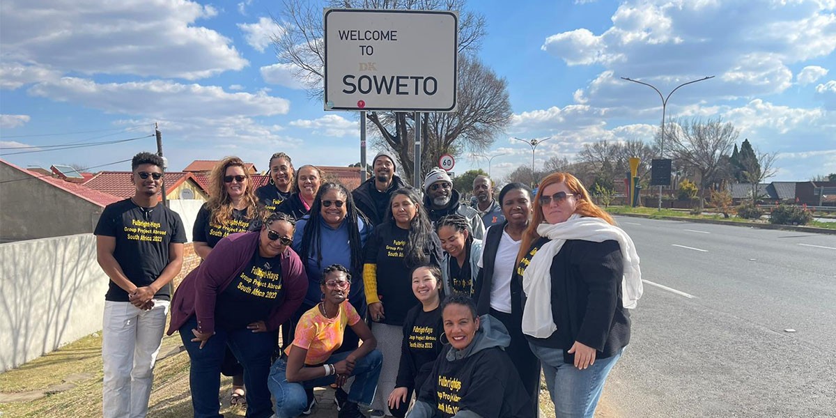  Fulbright-Hays GPA summer 2023 participants some kneeling, others standing in frony of Welcome to Soweto Sign inSoweto Township, South Africa 