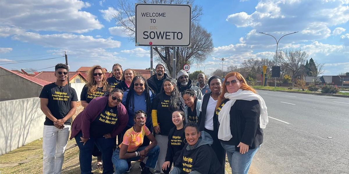 Fulbright-Hays GPA summer 2023 participants some kneeling, others standing in frony of Welcome to Soweto Sign inSoweto Township, South Africa