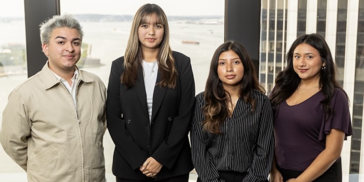 CREAR Futuros team standing in front of large office windows overlooking the water and nearby buildings.