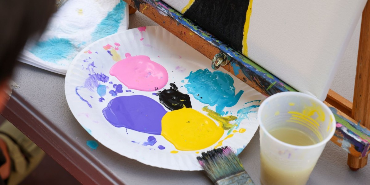 A paper plate with different color paint on it. Cup of water