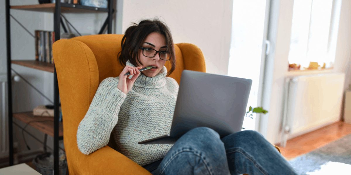 Female student in warm sweater on chair with laptop