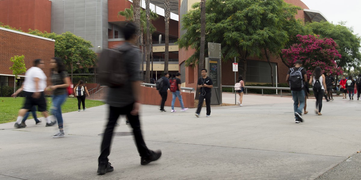 A student walking down a concrete walkway on campus.