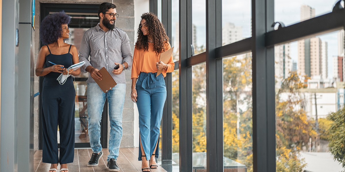 Three Co-workers walking down a windowed hallway. 