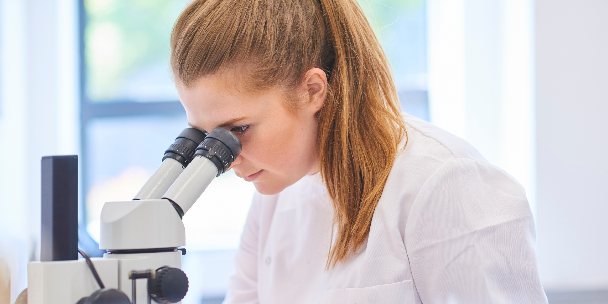 Woman in a lab coat looking through a microscope.