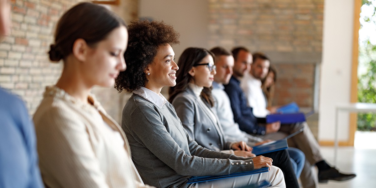 People sitting in a bright waiting room, focusing on one black woman.