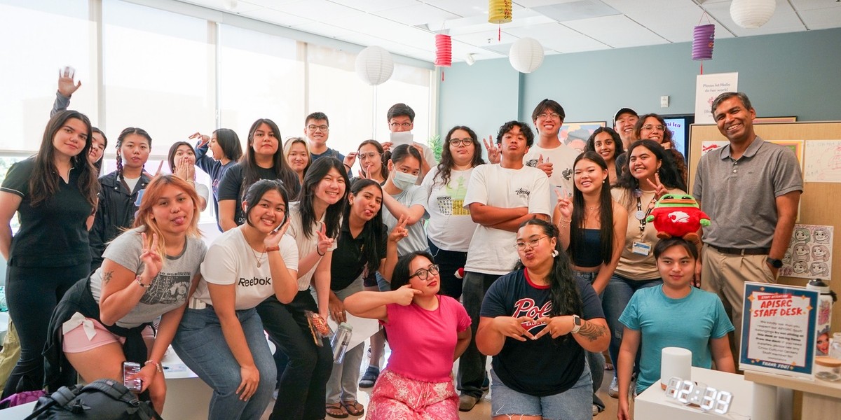 Roots Scholars gather for a group photo during the CommuniTEA Social at Cal State LA, posing cheerfully in a bright room decorated with colorful paper lanterns.