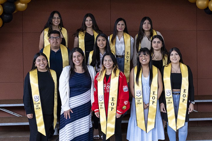 A group of students wearing gold graduation sashes standing in three rows.