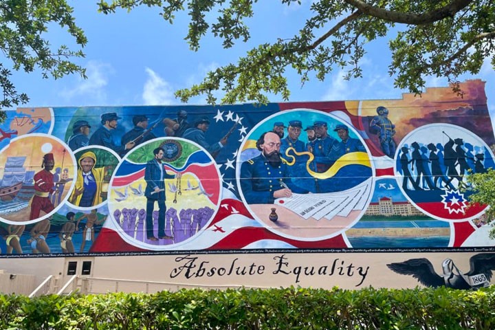 Colorful mural titled ‘Absolute Equality’ in Galveston, Texas, depicting scenes from Black history and Juneteenth, including enslaved people, Union soldiers, a central figure writing the emancipation order, and African American communities celebrating freedom, framed by an American flag motif.