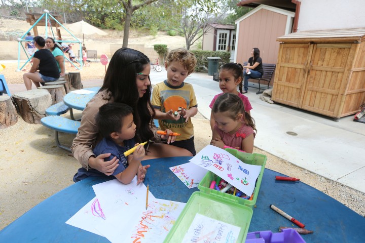 An adults sits with three children at a table outdoors.