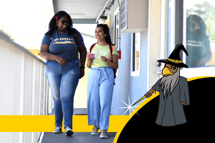 Two students laughing and walking together in front of Housing .Eddie the Golden Eagle dressed as a wizard.