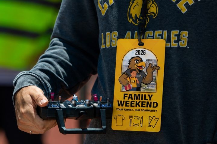 Person wearing a Cal State LA Family Weekend 2026 all-access badge while holding a remote controller.