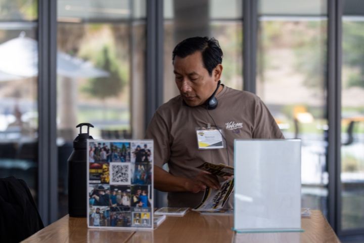 Man looking at flyers on a table. Brown shirt with a name tag.