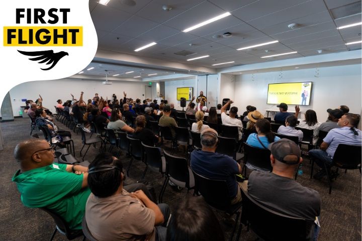 Multiple families and supporters in a room during a past orientation session, First Flight Logo seen at the top right which includes text: First Flight and a shadow of  a golden eagle