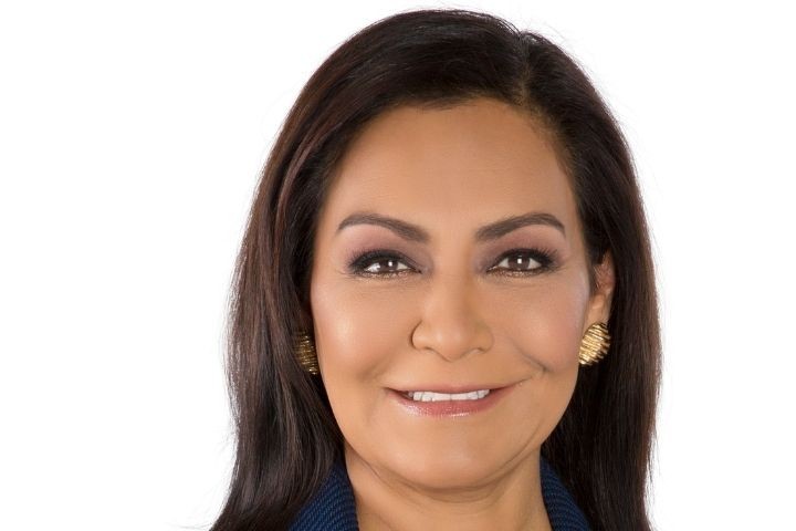 Headshot of woman with blue blazer, dark hair and gold earrings