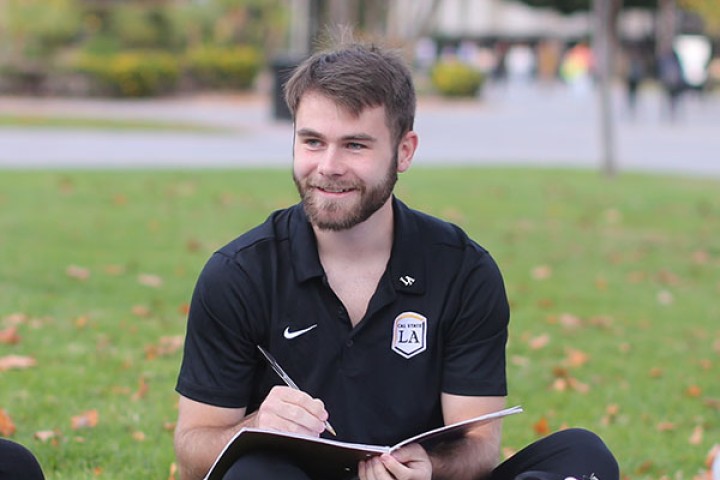 Student holding notebook and pen sitting on lawn