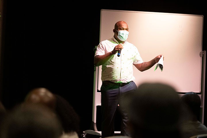 Person in mask onstage addressing audience