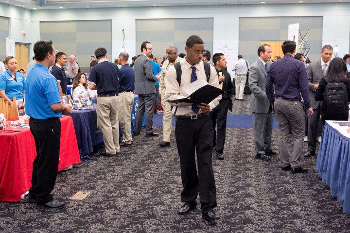 Student in professional clothing walks down career fair aisles confidently