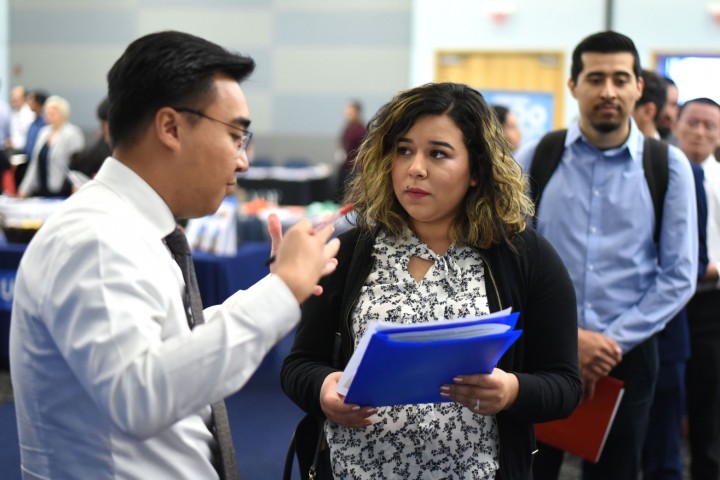 Student holding a portfolio speaks with employer at the career fair. 