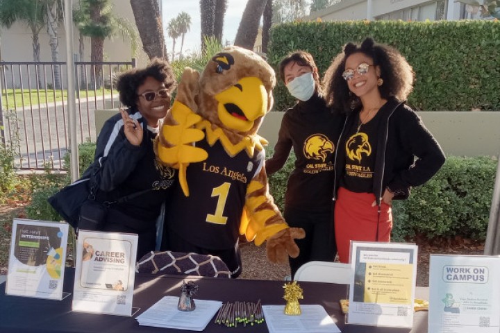 Career advisors, students and campus mascot Eddie smile while at a booth outside the Career Center