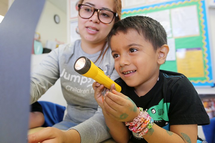 Child sitting next to teacher holding up a flashlight