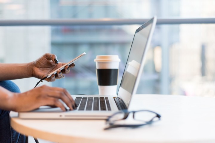 Womans hands holding a phone over  a laptop