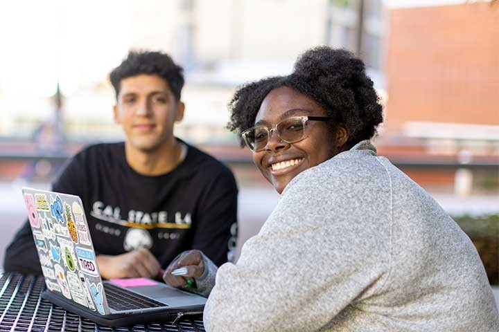 Two students smiling while studying with a laptop