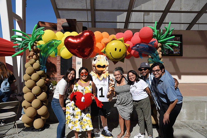 Group of people leaning in, posing in front of a large tropical balloon display.