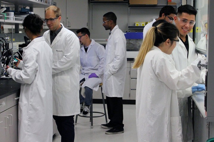 faculty, students in lab coats and safety glasses work in lab
