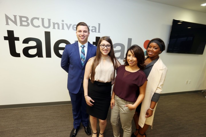 Four students wearing business attire stand in front of a wall with an NBC Universal sign.