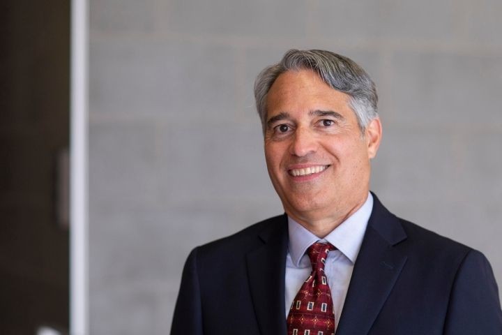 Man with gray hair with dark blue suit, red tie and light blue shirt