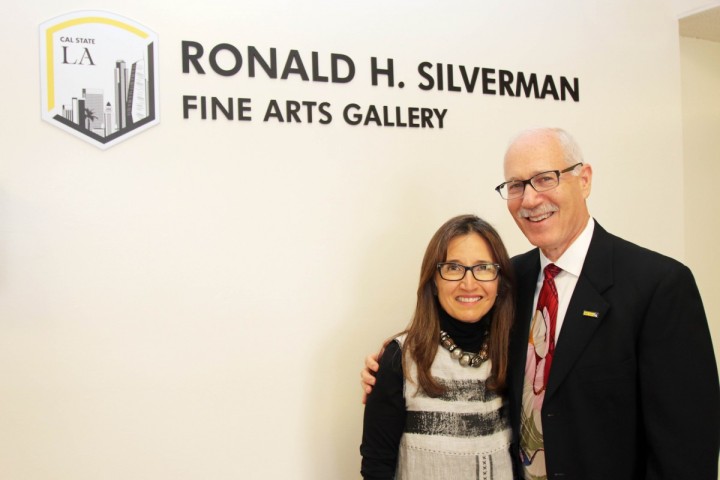 Two people smiling while standing in front of the Ronald H. Silverman Fine Arts Gallery