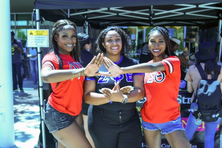 Three people wearing t-shirts with Greek letters smiling.