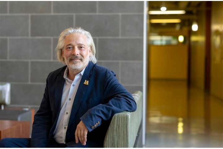 Portrait of Stephen Trzaskoma seated on a bench inside a modern campus building at Cal State LA, with tiled walls and a hallway in the background.