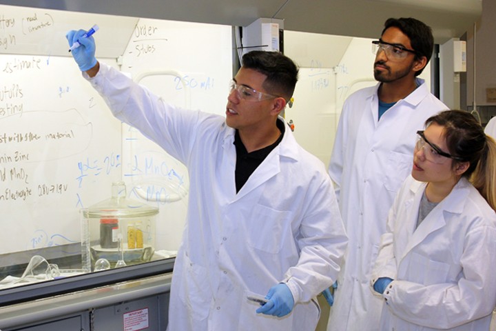 students in lab coats and goggles in lab working on formula