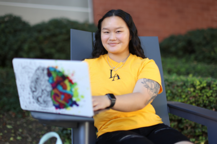 Female student sitting in lounge chair outside with open laptop.