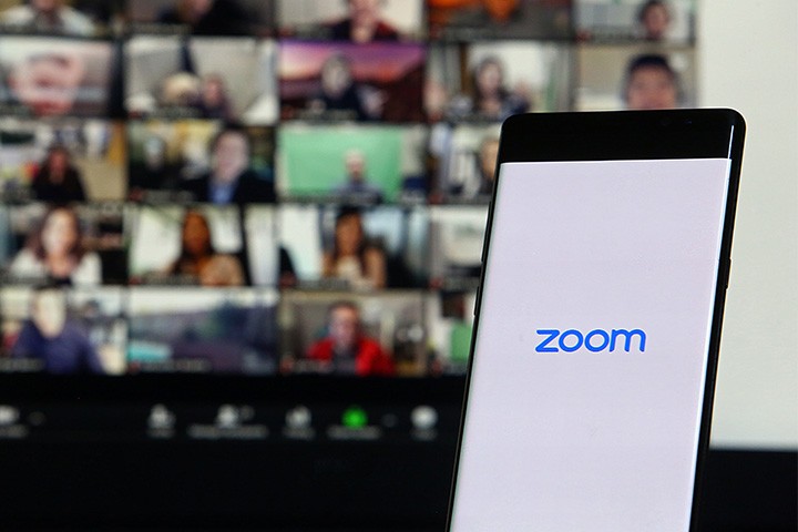 Virtual meeting participants in the background and a phone screen with the Zoom company logo