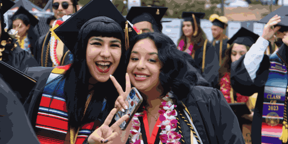 Two Cal State LA graduates in cap and gown celebrate together during graduation ceremony.