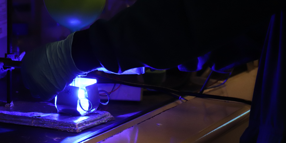 blue laser shines beneath gloved students hands in dark lab