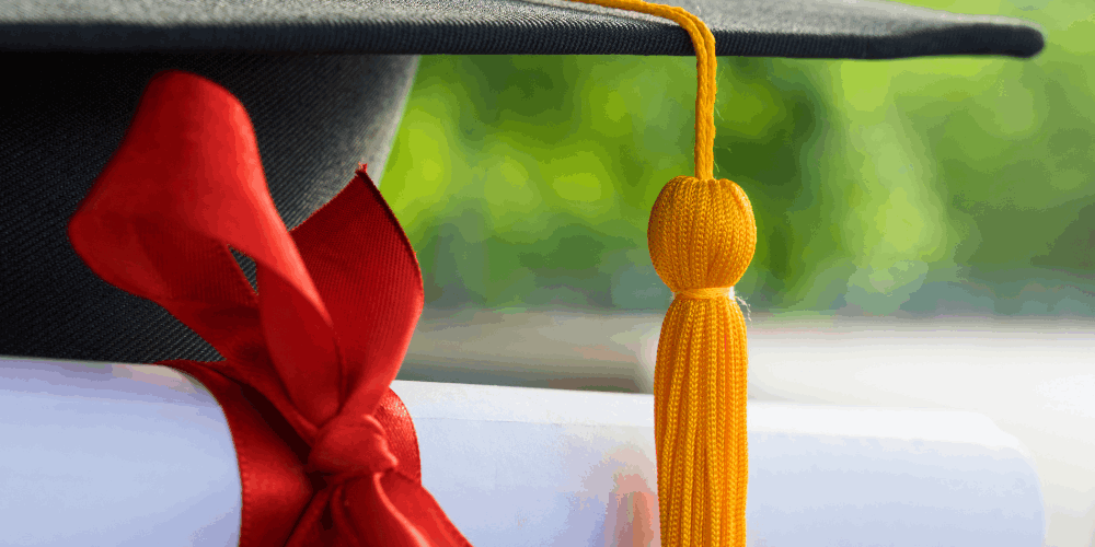 Black graduation cap with yellow tassel. White scroll with red ribbon.