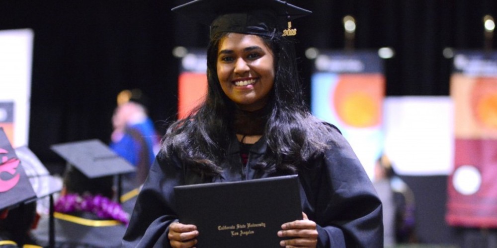 A graduate of Cal State LA at graduation, smiling, holding her diploma