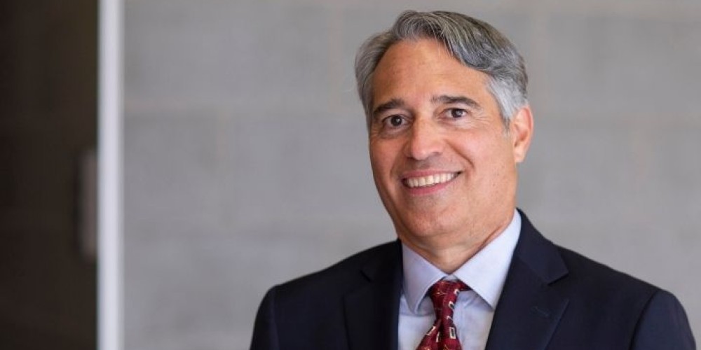 Man with gray hair with dark blue suit, red tie and light blue shirt