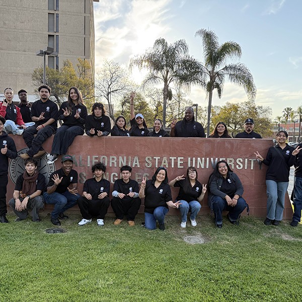 A group of people standing or sitting around an outdoor sign for California State University Los Angeles