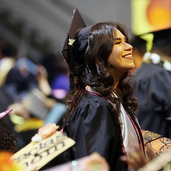 Graduating student in cap and gown smiles and looks in distance