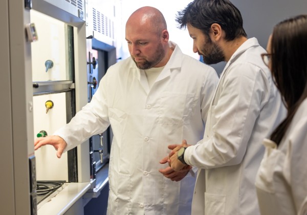Petr Vozka and two researchers in white lab coats examine laboratory equipment.