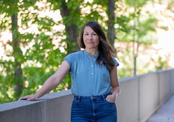 Student wearing a blue top and jeans standing outside with trees in the background